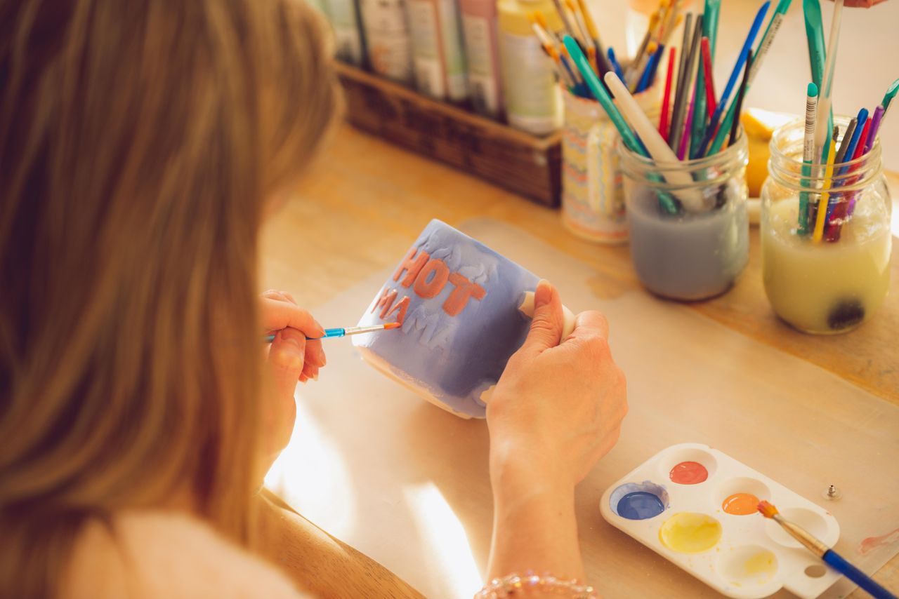 gallery-03 Close-up of a woman painting a mug in an art studio with bright colors.