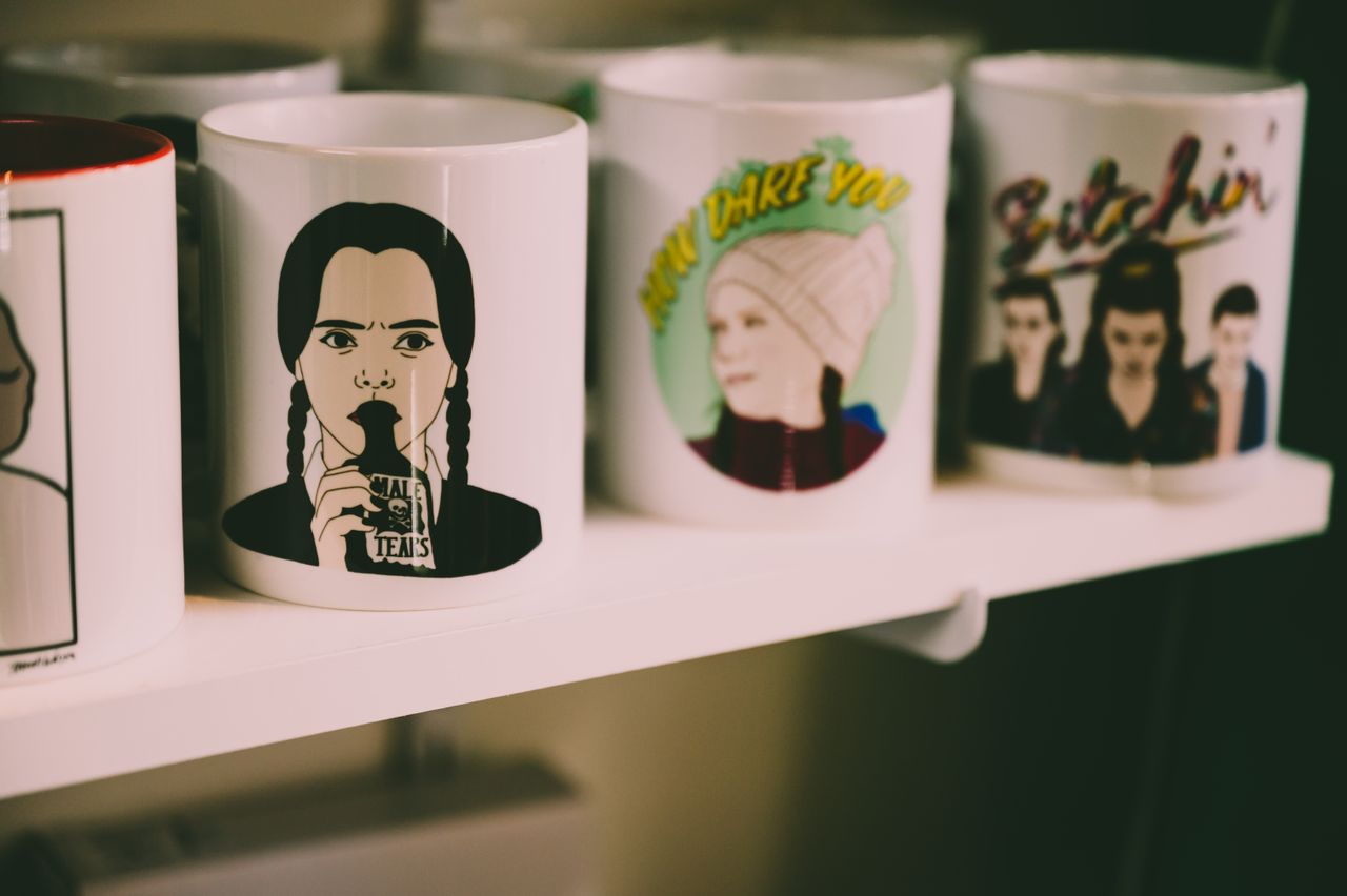 home-img A collection of artistic ceramic mugs featuring graphic designs displayed on a shelf.